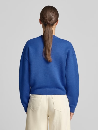 Frauenmodel trägt Strickjacke mit Brusttaschen von Rich & Royal in Blau, lockere Passform, gerippte Abschlüsse, Ganzkörperansicht Rückansicht.