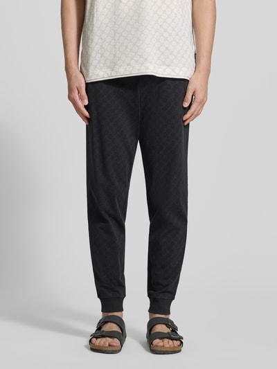 Männermodel trägt Sweatpants mit Logo-Muster und elastischem Bund von JOOP! Collection aus reiner Baumwolle, Regular Fit, Ganzkörperansicht von vorne.
