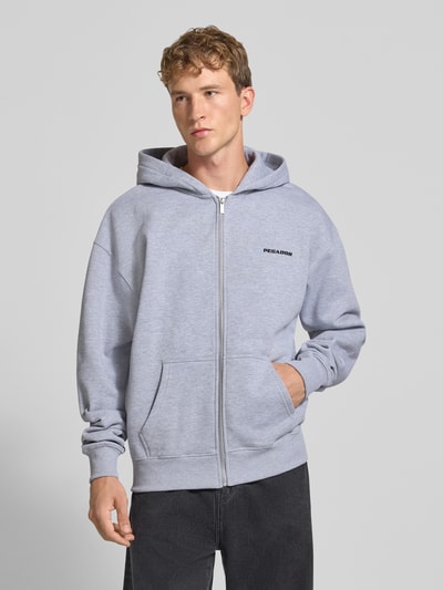 Männermodel trägt Regular Fit Sweatjacke aus Baumwoll-Mix von PEGADOR in Hellgrau mit Logo-Stickerei, Kängurutasche, Zipper, Ganzkörperansicht von vorne.