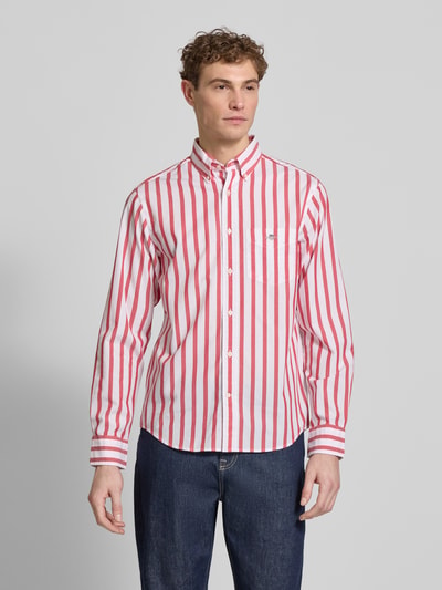 Männermodel trägt Slim Fit Freizeithemd mit Brusttasche von Gant in Rot-Weiß gestreift, aus reiner Baumwolle, Ganzkörperansicht von vorne.