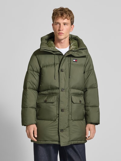 Männermodel trägt Parka mit Logo-Patch Modell 'WORKWEAR' von Tommy Jeans in Olivgrün, Steppstruktur, Pattentaschen, Ganzkörperansicht von vorne.
