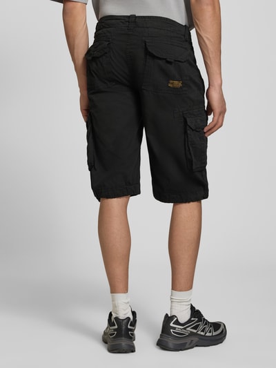 Männermodel trägt Bermudas mit Pattentaschen und Logo-Stitching von Alpha Industries aus Reine Baumwolle, Straight Fit, Ganzkörperansicht Rückansicht.