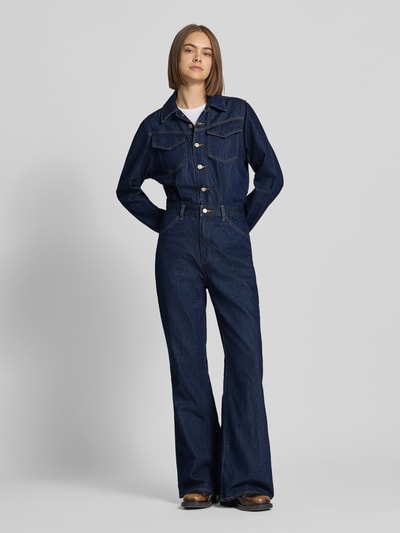 Frauenmodel trägt Regular Fit Jumpsuit aus reiner Baumwolle von Levi's® 300 in Dunkelblau, weiße Knöpfe, Ganzkörperansicht von vorne.