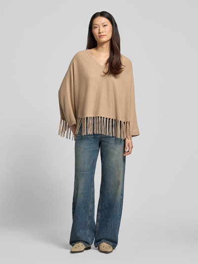 Frauenmodel trägt Relaxed Fit Pullover aus Woll-Mix mit Kaschmir-Anteil von HERZENS, beige, Fransen-Abschluss, Strick-Optik, V-Ausschnitt, langärmelig, Ganzkörperansicht von vorne.