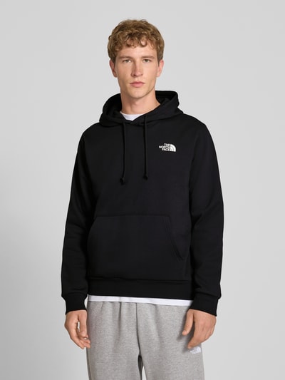 Mannelijk model draagt Regular Fit Hoodie met kap Model "EVOLUTION BOX" van The North Face in zwart katoenmix met kangoeroezak, capuchon met tunnelkoord, elastische boordjes, ruglengte maat M 67 cm, mouwlengte maat M 68 cm, vooraanzicht bovenlichaam.
