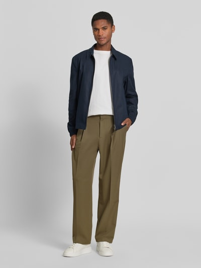 Männermodel trägt Stoffhose mit Bügelfalten und Eingrifftaschen von MCNEAL in Olive, Material-Mix mit Viskose-Anteil, Loose-Fit, Knopf-Reißverschluss, Bundweite 34 cm, Innenbeinlänge 80 cm, Ganzkörperansicht von vorne.
