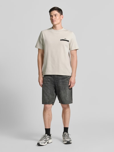 Męski model nosi t-shirt z nadrukiem na plecach model 'Bobby' od Wood Wood, bawełna, krój regular fit, okrągły dekolt, nadruk z logo, długość tyłu w rozmiarze M: 70 cm, jasne kolory, proste formy, gładka faktura. Ganzkörperansicht von vorne.