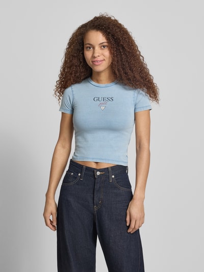 Frauenmodel trägt Cropped Damen T-Shirt aus Baumwoll-Elasthan-Mix, Logo und Rundhalsausschnitt, Modell 'BABY BAKER TEE' von Guess Jeans, Ganzkörperansicht von vorne. Rückenlänge bei Größe S: 42 cm.