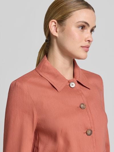 Frauenmodel trägt langärmlige, rostfarbene Bluse mit Kragen und großen Knöpfen, glatte Struktur, Nahaufnahme Oberkörper.