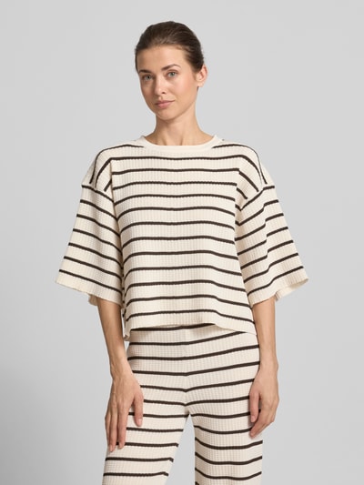 Frauenmodel trägt Oversized T-Shirt aus Viskose-Mix Modell 'NURIA' von VILLA SOPHIE, Optik: Allover-Muster, Passform: Oversized, Label-Applikation, Kragenform: Crew Neck, Ausschnitt: Rundhals, Ärmelform: Kurzarm, Materialverarbeitung: Rippstrick, Material: Viskose-Mix, in creme mit braunen Streifenstruktur, Ganzkörperansicht von vorne.