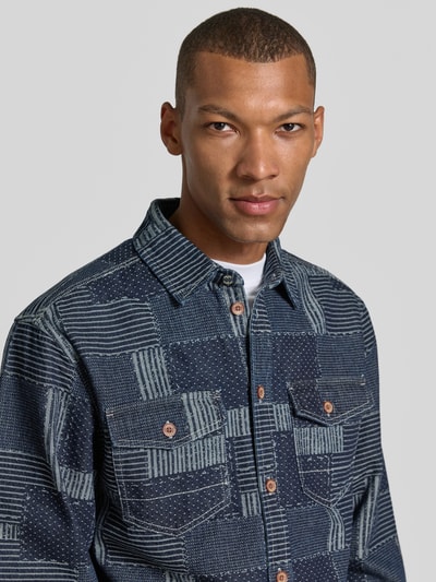 Männermodel trägt Relaxed Fit Hemdjacke in Denim-Optik von Scotch & Soda, Patchwork-Design in Blau, reine Baumwolle, Nahaufnahme Oberkörper