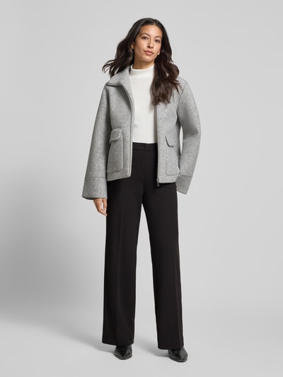 Frauenmodel trägt Wide Leg Bundfaltenhose mit Eingrifftaschen Modell 'Hillda' von STEHMANN aus Material-Mix mit Stretch-Anteil, schwarze Farbe, Knopf- und Reißverschluss, Bundfalten, Ganzkörperansicht von vorne.