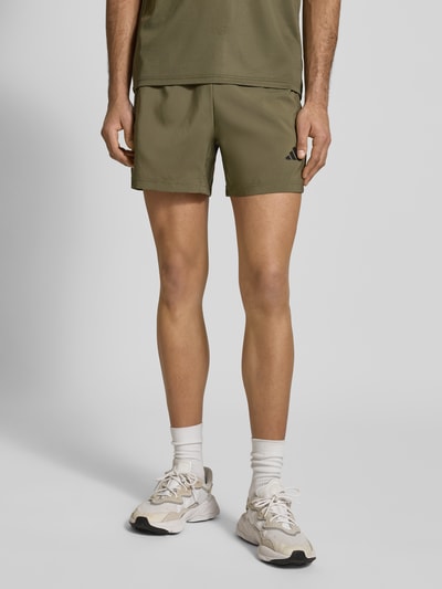 Männermodel trägt Shorts mit elastischem Bund von adidas Training in Khaki mit Label-Print, Reißverschlusstaschen, Lockerer-Schnitt, Ganzkörperansicht von vorne.