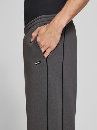 Männermodel trägt Straight Fit Sweatpants aus reiner Baumwolle mit Label-Patch von REVIEW in Dunkelgrau, Nahaufnahme Oberschenkel, Kontext: elastischer Bund, Eingrifftaschen, Innenbeinlänge Größe M 40 cm.