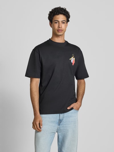 Männermodel trägt Boxy Fit T-Shirt aus reiner Baumwolle Modell 'FRED ESCAPE' von Only & Sons, unifarben schwarz mit Motiv-Print, Rundhals, kurzarm, Jersey-Material, Ganzkörperansicht von vorne.