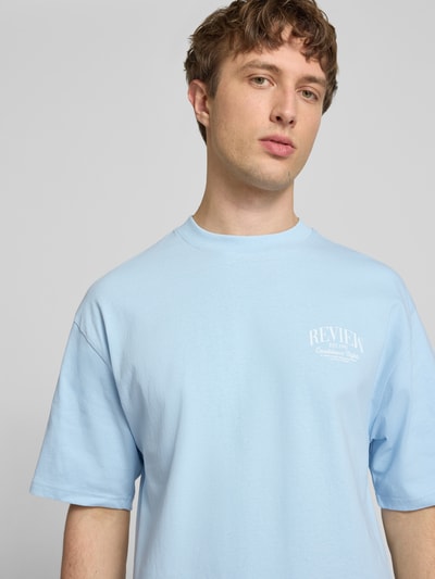 Männermodel trägt T-Shirt mit Label-Detail von REVIEW in Hellblau, Reine Baumwolle, Lockerer-Schnitt, Rundhalsausschnitt, 1/2-Arm, Nahaufnahme Oberkörper.