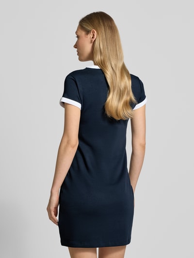 Frauenmodel trägt Slim Fit Minikleid mit Logo-Stitching Modell 'Mila' von Guess Activewear in Dunkelblau mit weißen Details, Rückansicht. Elastischer Baumwoll-Mix, kurzärmelig, Rundhalsausschnitt.
