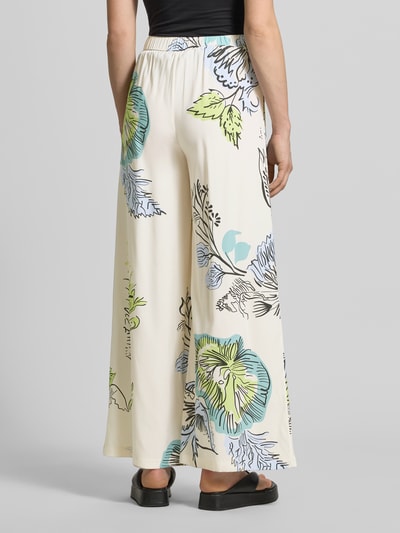 Frauenmodel trägt Stoffhose aus Seide-Mix von HERZENS, mit floralem Muster in Creme, Grün, Blau, Loose-Fit, elastischer Bund, Tunnelzug, Damen, Bundweite bei Größe 36 37 cm, Innenbeinlänge 76 cm, Ganzkörperansicht Rückansicht.