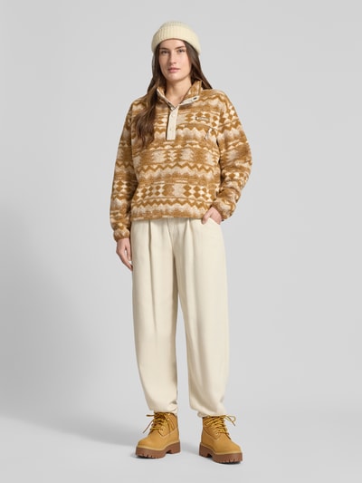 Modelka kobieca nosi Regular Fit Pullover mit Logo-Patch Modell 'Helvetia' od COLUMBIA, wzór w odcieniach brązu, z kieszenią na piersi, krój regular fit, materiał o fakturze polaru, widok całej sylwetki z przodu.