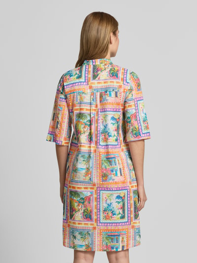 Frauenmodel trägt Knielanges Kleid aus reiner Viskose von Emily Van den Bergh mit buntem Muster, Stehkragen, Knopfleiste, 3/4-Arm, lockere Passform, Rückenlänge 103 cm bei Größe 36, Brustweite 49 cm, Ärmellänge 40 cm, Ganzkörperansicht Rückansicht.
