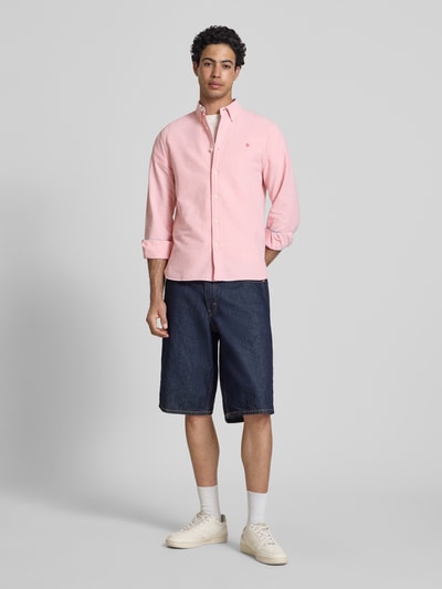 Męski model nosi Regular Fit Freizeithemd mit Logo-Stitching od Superdry, jasnoróżowa bawełna, zapięcie na guziki, widok całej sylwetki z przodu, krój regular fit, kołnierzyk button-down, mankiety sportowe, długość tyłu w rozmiarze M: 73 cm, szerokość ramion w rozmiarze M: 40 cm, długość rękawa w rozmiarze M: 63 cm