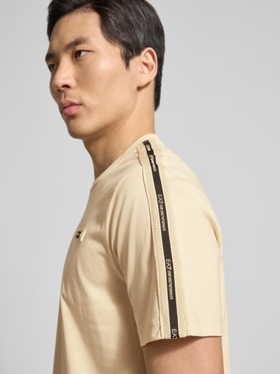 Männermodel trägt Regular Fit T-Shirt mit Logo-Patch von EA7 Emporio Armani aus beige Baumwolle, Rundhalsausschnitt, Nahaufnahme Oberkörper.