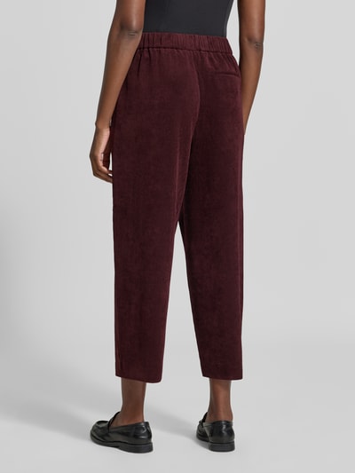 Frauenmodel trägt Wide Fit Hose in Cord-Optik Modell 'Cisilia' von someday in dunklem Rot, elastischer Bund, strukturierte Oberfläche, Ganzkörperansicht Rückansicht, Damen Hose, verkürzte Passform, Material-Mix, Größe 36.