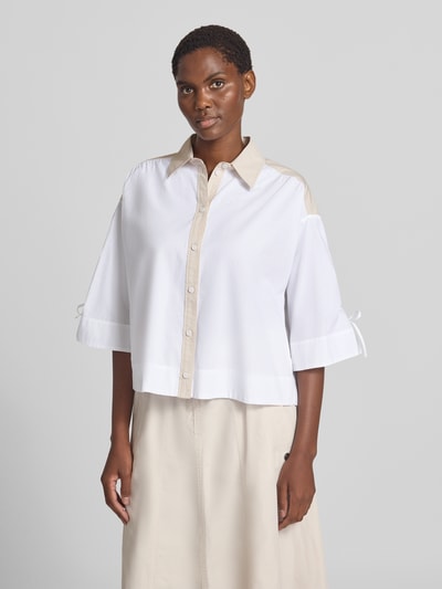 Frauenmodel trägt Boxy Fit Bluse mit 3/4-Arm von Marc Cain in Weiß-Beige, reine Baumwolle, Hemdblusenkragen, Knopfleiste, Ganzkörperansicht von vorne.