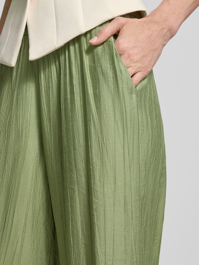 Frauenmodel trägt Wide Leg Culotte aus Viskose-Mix von s.Oliver RED LABEL in Hellgrün, Crêpe-Textur mit seitlicher Eingrifftasche, Nahaufnahme Oberschenkel.