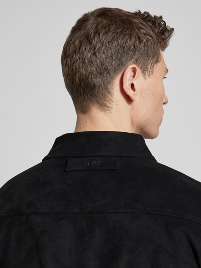 Männermodel trägt Regular Fit Freizeithemd in Wildleder-Optik Modell 'ENASO' von HUGO, schwarze Oberfläche, Ganzkörperansicht Rückansicht. Herrenhemd mit Kentkragen, einreihiger Knopfleiste und seitlichen Eingrifftaschen, strukturierte Textur.