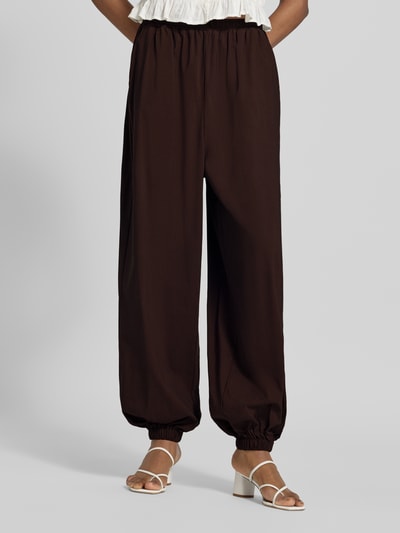 Frauenmodel trägt Balloon Fit Stoffhose aus Viskose-Mix Modell 'Hamy' von FREE/QUENT in Dunkelbraun, glatte Struktur, Nahaufnahme Unterkörper, elastischer Bund mit Tunnelzug, Eingrifftaschen und elastische Beinabschlüsse, Stoffhose wirkt leicht und locker, Kontext: Damen Stoffhose, Viskose-Elasthan-Mix, Balloon Fit, Bundweite S 37 cm, Innenbeinlänge S 74 cm.