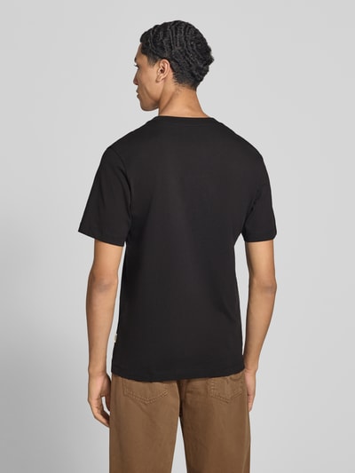 Męski model nosi t-shirt z nadrukiem z logo Model 'FREDERIKSBERG' od JACK & JONES z czarnej bawełny, prosty krój, okrągły dekolt, długość tyłu w rozmiarze M: 70 cm, widok całej sylwetki od tyłu