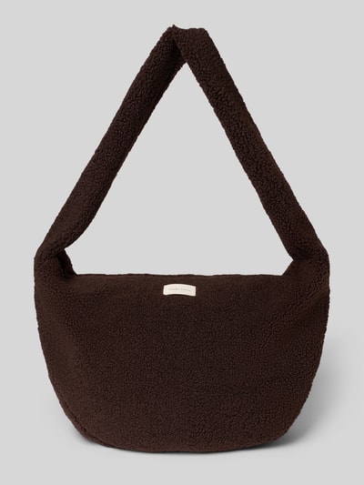 Produktfoto, Crossbody Bag aus Teddyfell von Studio Noos in Dunkelbraun, sichtbarer Logo-Patch, grobe Struktur, rechteckige Form, grauer Hintergrund. Hauptfach mit Reißverschluss, Schulterriemen, Maße: 58x35x11 cm, Länge Schulterriemen 80 cm.