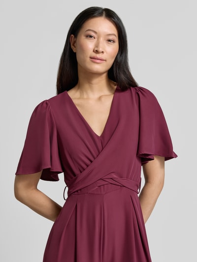 Frauenmodel trägt Jumpsuit mit Stoffgürtel von Rinascimento in Bordeaux, fließender Stoff, V-Ausschnitt, Kurzarm, Nahaufnahme Oberkörper.