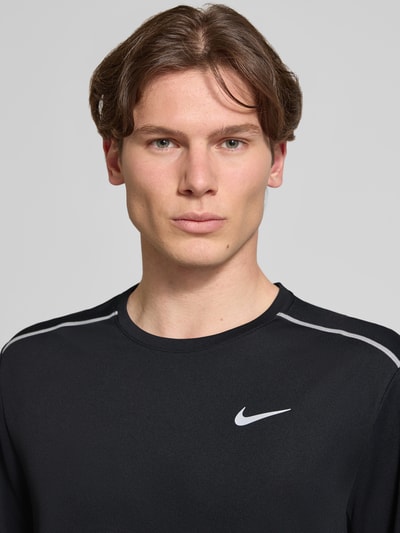 Männermodel trägt T-shirt mit ronde hals en logoprint van NIKE TRAINING in zwart met contraststrepen, regular fit, nahaufnahme oberkörper. Ruglengte maat M: 74 cm.