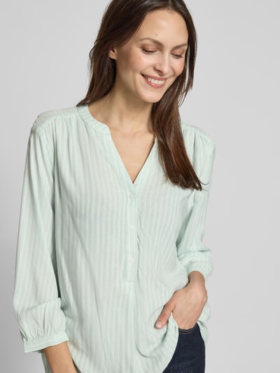 Frauenmodel trägt Comfort Fit Langarmbluse aus reiner Viskose von Tom Tailor mit Allover-Muster, Mao-Kragen, Tunika-Ausschnitt, Knopfleiste, 3/4-Arm, Manschette, blassgrün, Ganzkörperansicht von vorne.