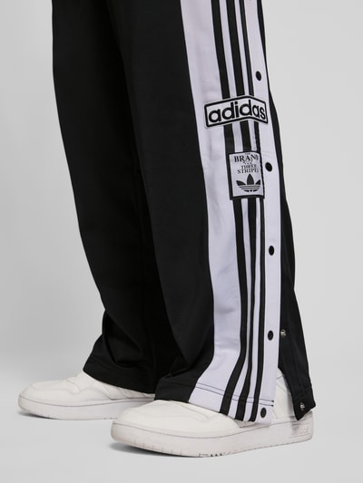 Männermodel trägt Trainingshose mit Label-Details und elastischem Bund von adidas Originals, schwarz-weiß, Relaxed-Fit, Detailaufnahme.