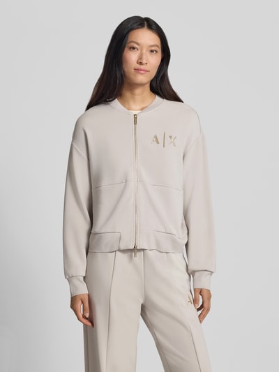 Frauenmodel trägt Sweatjacke mit Label-Print von Armani Exchange in Beige, lockere Passform, Zweiwege-Reißverschluss, Ganzkörperansicht von vorne.