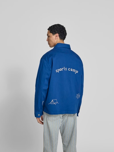 Männermodel trägt Hemdjacke mit Motiv-Stitching von Forét in Blau, aus elastischem Baumwoll-Mix, Relaxed-Fit, Ganzkörperansicht Rückansicht. Rückenlänge bei Größe M: 73 cm, aufgesetzte Taschen, durchgängige Knopfleiste, Motiv-Stitching auf dem Rücken.