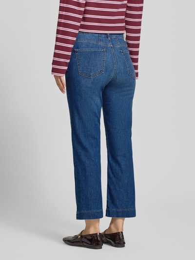 Frauenmodel trägt Bootcut Jeans im 5-Pocket-Design Modell 'Mary' von Brax aus blauem Baumwoll-Mix mit Stretch-Anteil, ausgestellter Schnitt, Label-Detail, Ganzkörperansicht Rückansicht.