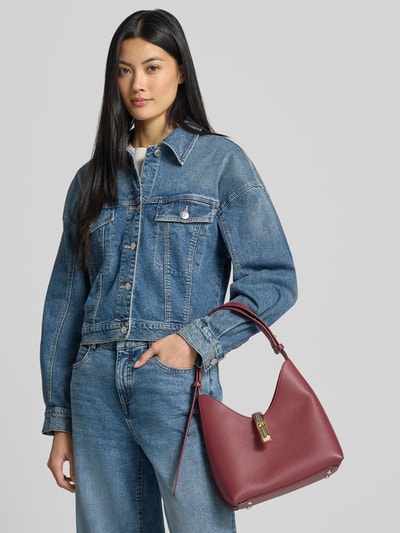 Frauenmodel trägt Handtasche aus echtem Leder Modell 'GOCCIA' von FURLA in Dunkelrot mit Strukturmuster, Überschlag und Pinschließe, Hauptfach, Innenfach mit Reißverschluss, verstellbarem Schulterriemen, Ganzkörperansicht von vorne.