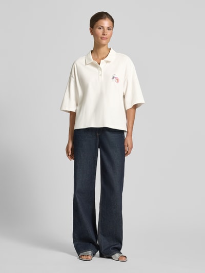 Frauenmodel trägt Cropped Poloshirt mit Ziersteinbesatz von Smith and Soul, Damen Poloshirt aus elastischem Baumwoll-Mix in Creme mit Polokragen, Halbarm und lockerer Passform, kombiniert mit dunkler Wide-Fit-Jeans, Ganzkörperansicht von vorne.