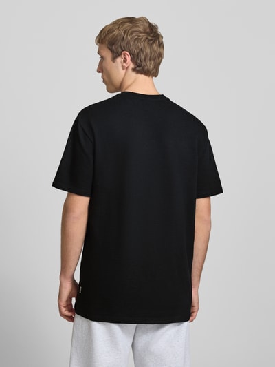 Männermodel trägt Regular Fit T-Shirt aus Baumwoll-Mix Modell 'KIAN' von Only & Sons, schwarz, Piqué-Struktur, Ganzkörperansicht Rückansicht.