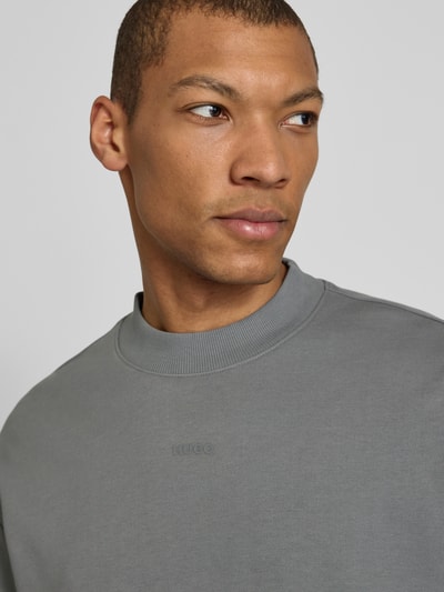 Männermodel trägt Regular Fit Sweatshirt aus reiner Baumwolle Modell 'DAPOCREW' von HUGO in Grau mit Rundhals, Nahaufnahme Oberkörper.