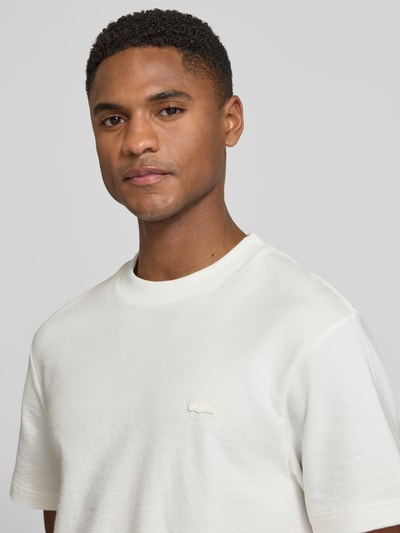 Männermodel trägt Regular Fit T-Shirt aus reiner Baumwolle von Lacoste in Weiß, unifarben, Label Patch, feinstrukturiert, Nahaufnahme Oberkörper.