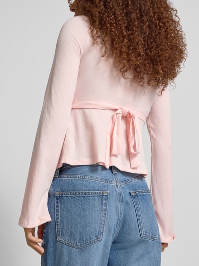 Frauenmodel trägt Regular Fit Langarmshirt in Wickel-Optik Modell 'PELLY' von Only, Struktur-Muster, Bindeband, Trompetenärmel, Ganzkörperansicht Rückansicht.
