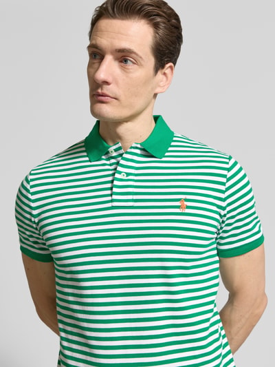 Männermodel trägt Slim Fit Poloshirt aus reiner Baumwolle von Polo Ralph Lauren mit Optik: Unifarben, Two-Tone, gestreift, Logo-Detail, Polokragen, V-Ausschnitt, kurze Knopfleiste, Kurzarm, gerippter Ärmelabschluss, Rumpfabschluss mit Seitenschlitzen, asymmetrisch, Materialverarbeitung: Piqué, Ganzkörperansicht von vorne.