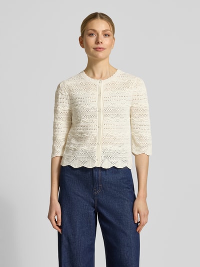 Modelka kobieca nosi Strickjacke mit Rundhalsausschnitt Modell 'GANACH' od SUNCOO PARIS, bawełna, krój regular fit, kremowy, przód z guzikami, faktura ażurowa, widok całej sylwetki z przodu.