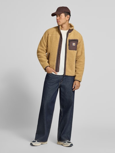 Männermodel trägt Teddyjacke mit Brusttasche Modell 'PRENTIS LINER' von Carhartt Work In Progress in Beige und Braun, Ganzkörperansicht von vorne. Regular Fit, Stehkragen, Reißverschlüsse, Label-Patch, geradlinige Textur.