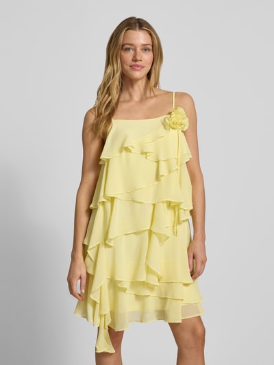 Vrouwenmodel draagt Fließendes Cocktailkleid mit Volants Modell 'ALADYN' van Vero Moda in uni geel met sierbloem, volantdetails, verstelbare spaghettibandjes, mini lengte, carré halslijn, soepel fit, voorkant bovenlichaam close-up.